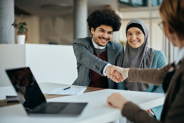 Young happy Muslim couple handshaking with insurance agent after signing contract in the office.