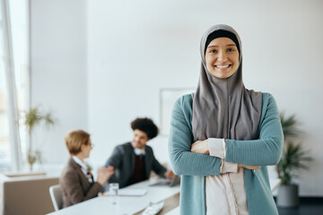 Portrait of confident Muslim businesswoman with crossed arms at corporate office.