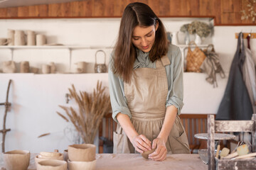 Master of art ceramics at work happy woman in an apron works in a ceramic workshop. The craftswoman creates handmade dishes in the workshop.