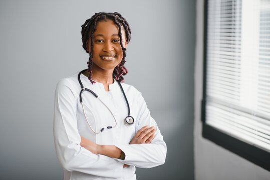 Portrait Confident African Female Doctor Medical Professional Writing Patient Notes Isolated On Hospital Clinic Hallway Windows Background. Positive Face Expression