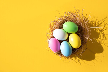 Top view of a nest with colorful eggs on a yellow background. Easter concept.