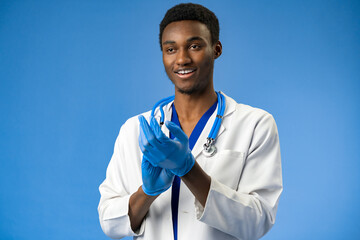 Young African American doctor putting on surgical gloves on blue background