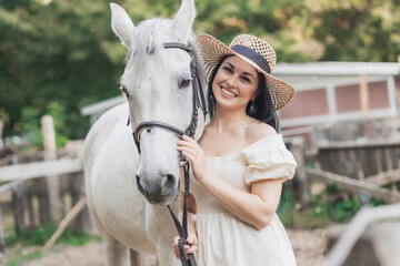 Piękna dziewczyna, w białej sukience i kapeluszu , z koniem na farmie  - obrazy, fototapety, plakaty