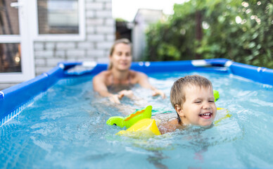 Mom plays with a naked baby in oversleeves in the pool against the background of a summer sunset