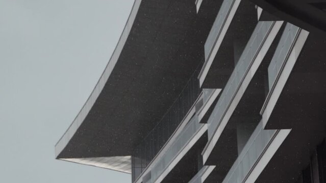 Small drops of heavy rain against the background of foggy cloud and the facade of modern building with gabled roof. It is raining in the city on cloudy day.