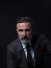 Portrait of a stylish elegant senior businessman with a beard and casual business clothes in photo studio isolated on dark background gesturing with hands