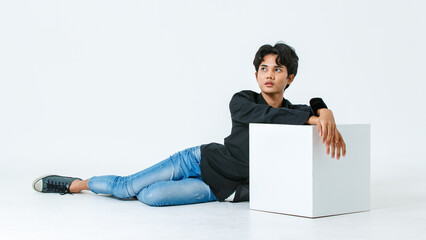 Portrait isolated cutout studio shot of Asian young LGBTQ gay glamour male model in casual black shirt and jeans outfit sitting stretching posing gesturing on floor look at camera on white background