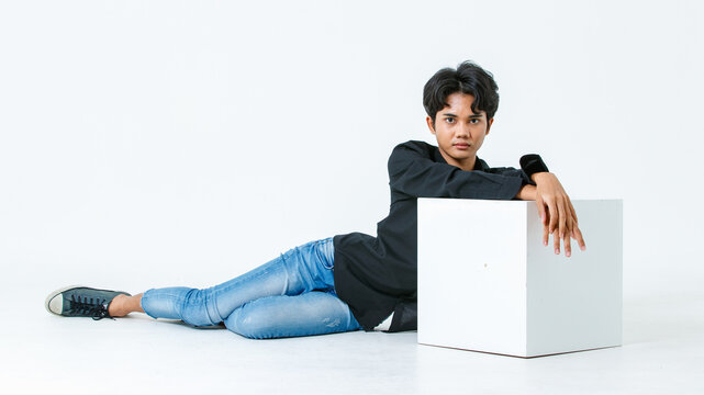 Portrait isolated cutout studio shot of Asian young LGBTQ gay glamour male model in casual black shirt and jeans outfit sitting stretching posing gesturing on floor look at camera on white background