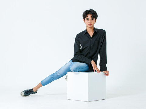 Portrait isolated cutout studio shot of Asian young LGBTQ gay glamour male model in casual black shirt and jeans outfit sitting stretching posing gesturing on floor look at camera on white background