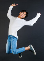 Studio shot of Asian young LGBTQ gay cheerful happy bisexual homosexual male model in casual outfit jumping high on air smiling laughing posing holding two fingers peace sign on black background
