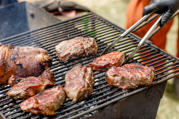 Close-up of meat steaks on the grill and barbecue with vegetables, corn.the chef holds the meat over the grill with tongs. food festival 