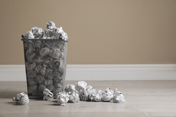 Trash bin full of paper on floor near beige wall, space for text. Recycling rubbish