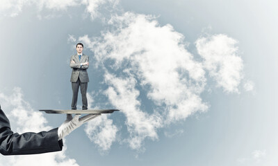 Confident businessman presented on metal tray against blue sky background