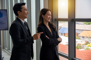 Smiling man and woman standing at meeting room beside windows.