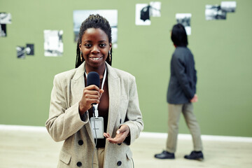 Horizontal medium portrait of young African American art gallery curator holding microphone...