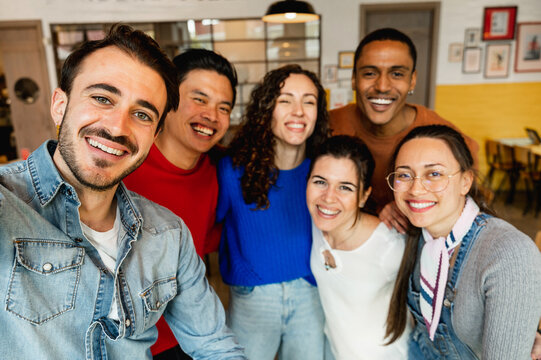 Group of six multiracial friends taking a selfie photo with smartphone in a restaurant.