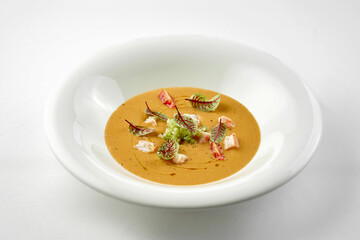 Close-up on pumpkin cream soup with crab in a white plate.