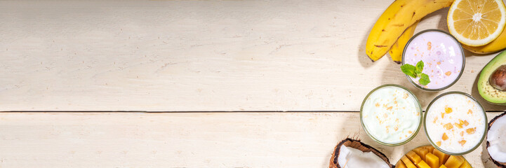 Refreshing yogurt, milkshakes or smoothies. Three glasses with fruit milkshakes. White banana, green apple avocado, yellow mango tropical fruits smoothie. On white wooden table, copy space