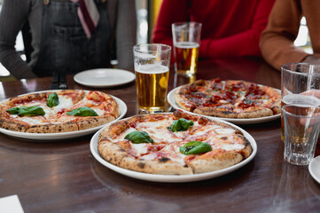 Close-up glasses of beer and pizzas on a table. Unrecognizable unfocused group of people on background.