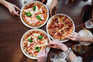 Top view three delicious Italian pizzas on table. Unrecognizable cropped people's hands taking a...