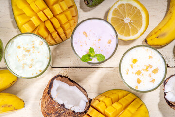 Refreshing yogurt, milkshakes or smoothies. Three glasses with fruit milkshakes. White banana, green apple avocado, yellow mango tropical fruits smoothie. On white wooden table, copy space