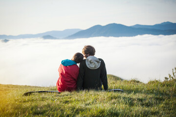 Fototapeta na wymiar Young Couple in Love Sitting at Dawn on a Meadow in the Carpathian Mountains