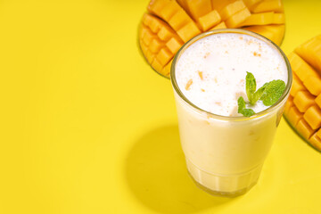 Fresh mango smoothie, yogurt, milkshake or smoothie with half slice of mango on high-colored bright background top view copy space