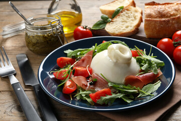 Delicious burrata salad with tomatoes, prosciutto and arugula served on wooden table