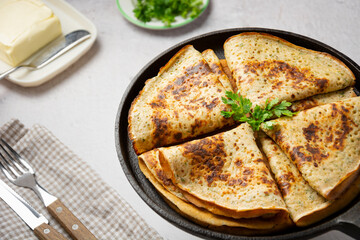 Thin cheese pancakes with greens, folded in a triangle in a cast iron pan, served with cutlery and...