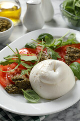 Delicious burrata salad with tomatoes, arugula and pesto sauce served on white marble table, closeup