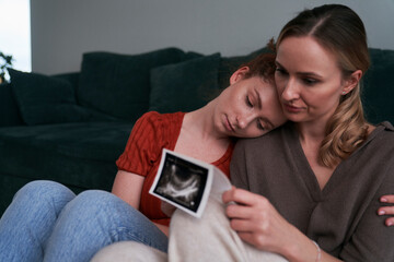 Woman holding ultrasound scan and being consoled by the best friend.