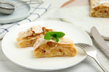 Pieces of delicious apple strudel with almonds, powdered sugar and mint on white wooden table