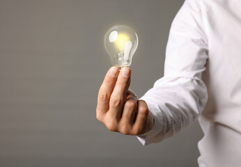 Glow up your ideas. Closeup view of man holding light bulb on grey background, space for text