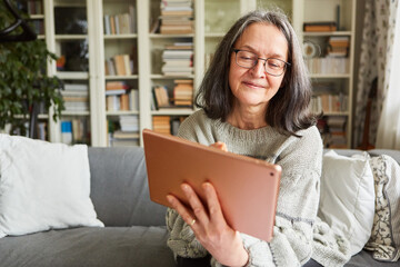 Elderly woman on the sofa using tablet computer online