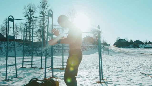 Bodybuilder without a t-shirt on a winter day preparing for training at the city sports ground in a park