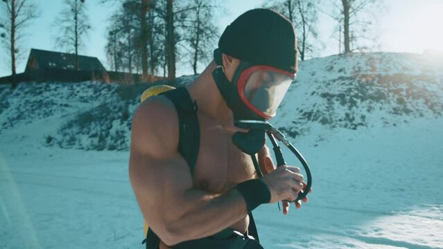 Bodybuilder a drager on his back puts on a full face mask and adjusts the pressure gauge while standing in a winter park