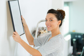 woman hanging picture on wall