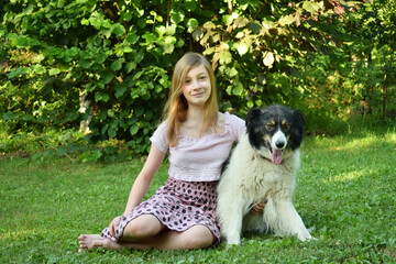 Girl playing with dog on grass. Teenager hugging Carpathian Shepherd Dog in the summer park. A Friendship concept of man and animal