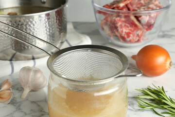 Straining delicious broth through sieve on white marble table, closeup