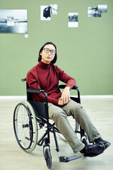 Portrait of handsome young Asian man with disability in wheelchair visiting contemporary photography exhibition in art gallery