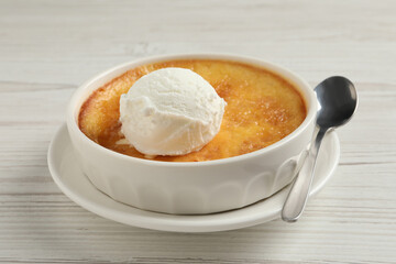 Delicious creme brulee with scoop of ice cream and spoon on white wooden table