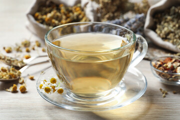 Glass cup of aromatic freshly brewed tea near different dry herbs on wooden table