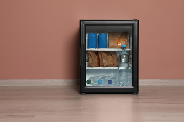 Mini bar filled with food and drinks near pale pink wall indoors, space for text