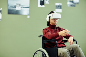 Horizontal medium shot of young Asian man with disability wearing VR headset visiting exhibition in modern art gallery using augmented reality technology