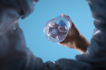 Bottom view of woman throwing plastic bottle into trash bin on light blue background, closeup