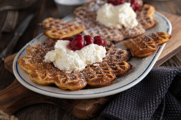 Heart shaped and round waffles with whipped cream and cherries. Fresh and homemade baked