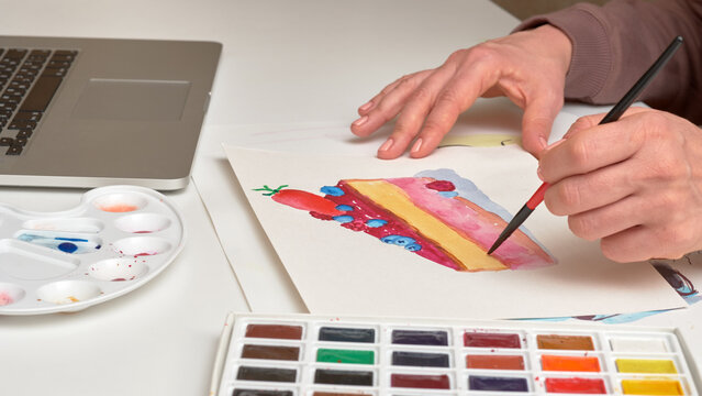 the artist's left hand holds brush for watercolors and paints the cake