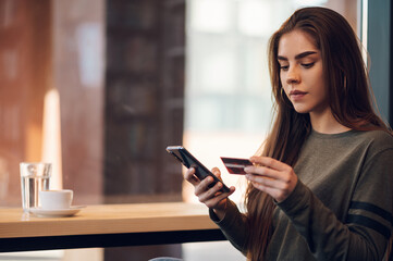 Woman using smartphone and a credit card for online shopping in a cafe