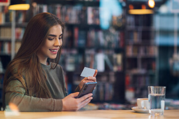 Woman using smartphone and a credit card for online shopping in a cafe