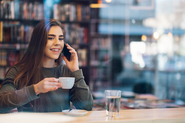 Woman using smartphone and drinking coffee in a cafe.